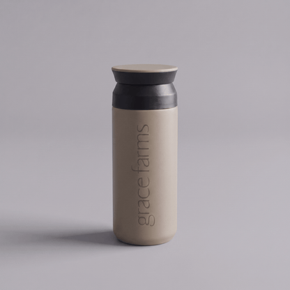 KINTO travel tumbler in sand beige, featuring the vertical white text 'grace farms' on the front, set against a solid gray background.